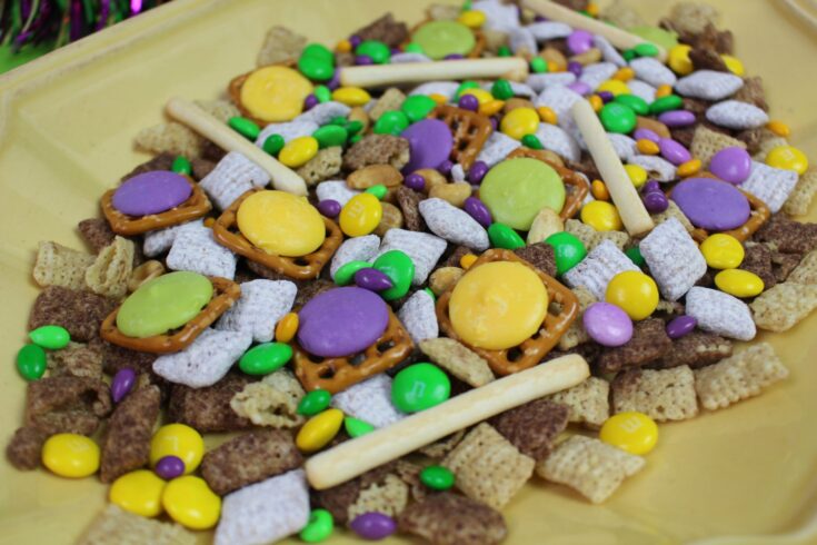 purple, green and yellow pretzel, chocolate and Chex cereal snack mix on yellow plate