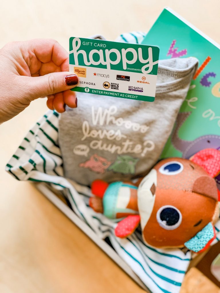 women holding happy gift card over baby gift with onesie and brown squirrel toy