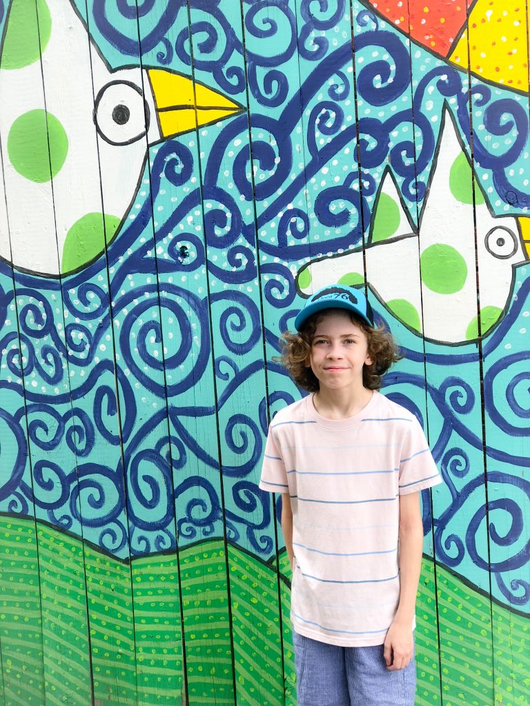 tween boy in pink shirt standing in front of blue and green mural