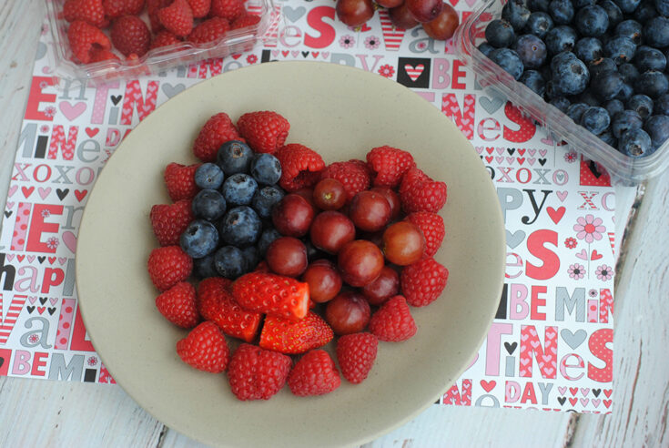 strawberries, raspberries, blueberries and grapes in heart shape on white plate