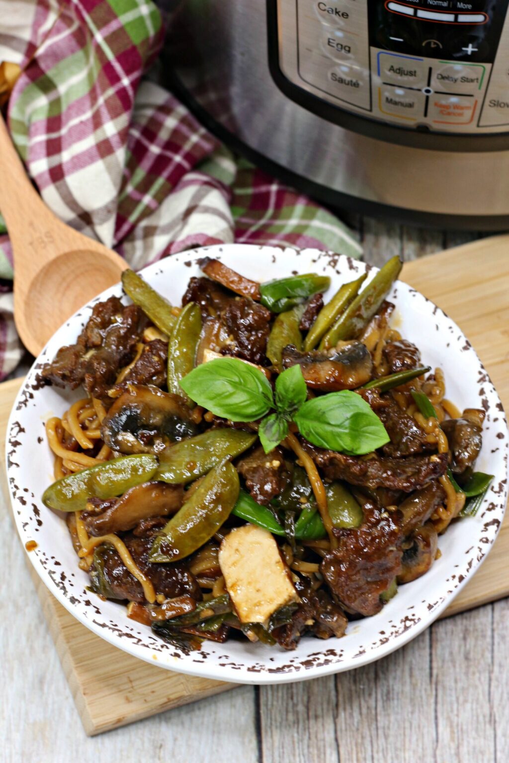 Thai steak in white bowl next to wooden spoon and burgundy plaid towel
